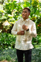 A man wearing a traditional Filipino Barong Tagalog shirt with embroidery, in a garden setting.