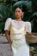Woman in a cream organza filipiniana top holding a woven basket with a natural background
