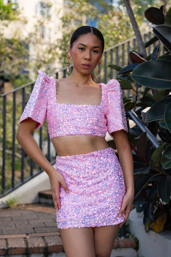 Woman wearing a pink sequin Filipiniana terno standing outdoors with plants in the background