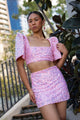 Woman wearing a pink sequin Filipiniana terno standing outdoors with plants and buildings in the background