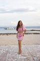 Woman in a pink sequin Filipiniana terno standing on a beach with ocean and sky in the background