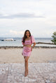 Woman in a pink sequin Filipiniana terno standing on a stone pathway by the beach