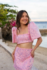Woman wearing a pink sequin Filipiniana terno standing by a waterfront.