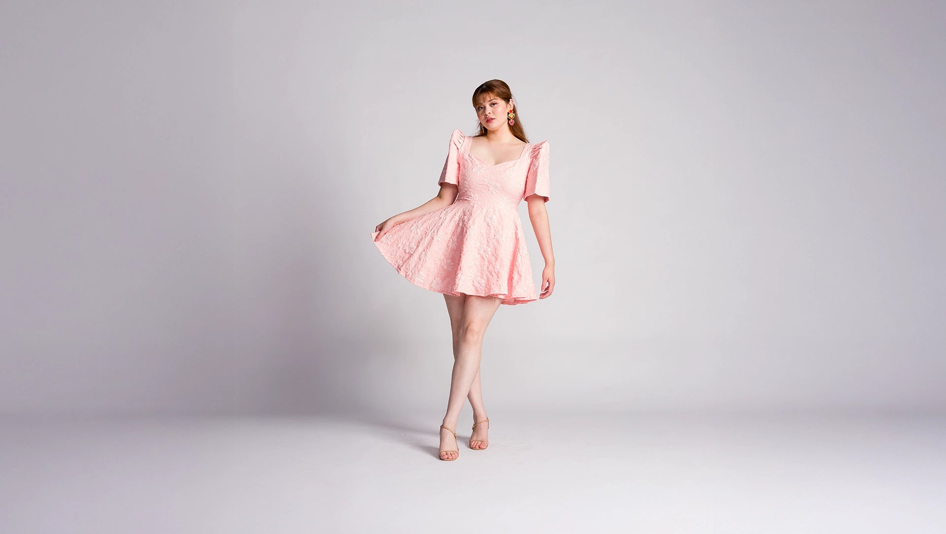 Filipina woman wearing a pink mini filipiniana dress with jacquard detail on a plain background