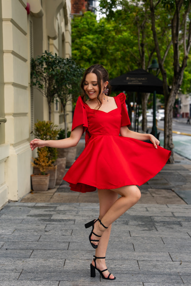 Modern Filipina woman wearing structured satin red mini filipiniana graduation dress with butterfly sleeves and heart cut-out back
