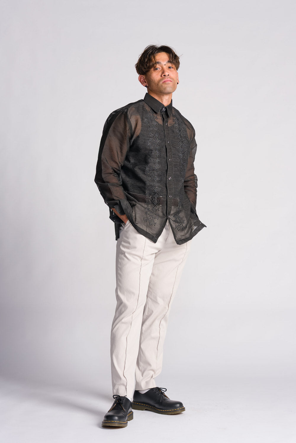 Man wearing a sheer black organza barong tagalog filipino formal shirt with light pants on a white background