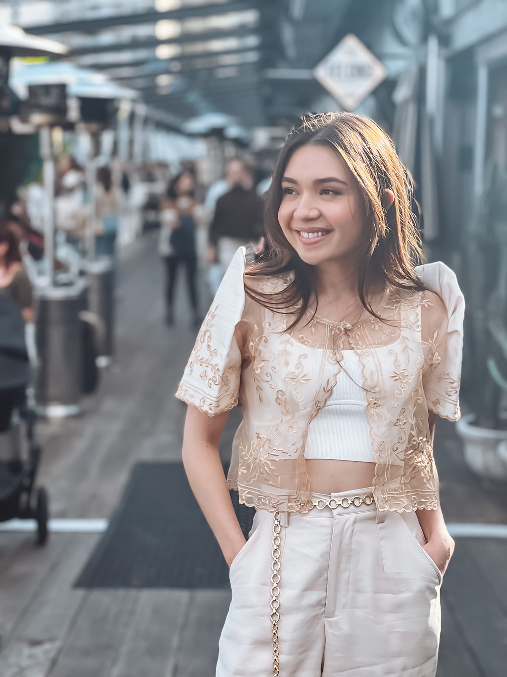 A woman wearing a cream-colored filipiniana bolero with floral embroidery over a white top, paired with light-colored pants.